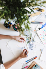 Close up girl hands drawing with colored felt-tip pens on paper at the desk