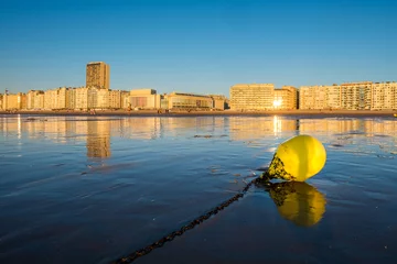 Foto auf Leinwand Bright yellow buoy on the beach of Oostende with city skyline in the background © Erik_AJV