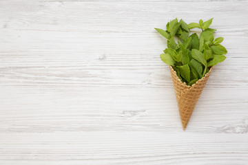 Waffle sweet ice cream cone with mint on white wooden background, top view. Flat lay, overhead, from above. Copy space.