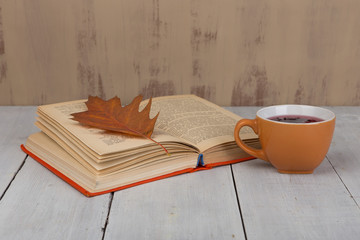 Concept of autumn resting - cup of tea with autumn colorful leaves and book on white wooden table and brown background