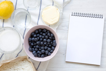 Top view, raw ingredients for cooking blueberry pie with notepad. Overhead, flat lay. Space for text.