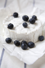 Camembert cheese in paper on striped napkin, closeup.