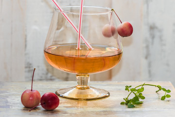Golden color drink in the cognac glass decorated with paradise apples, straws,  and spring of mint 