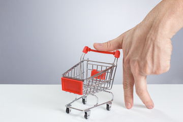 Male hand standing on two fingers and holding shopping cart on white background
