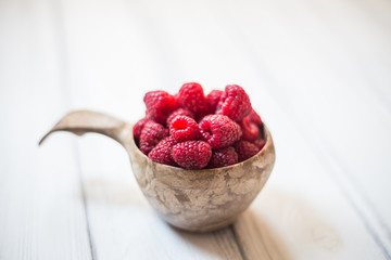 Wooden bowl with summer raspberries on white table