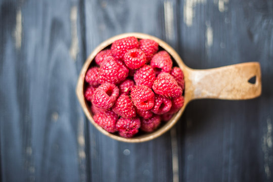 Wooden bowl with summer raspberries on wooden table close up