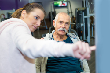 elderly man worming up at gym with female trainer