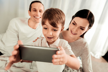 Fototapeta premium Modern technology. Cute positive boy taking photos while being together with his family
