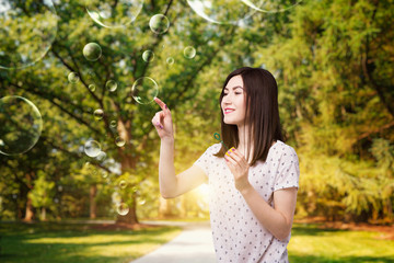 Cute woman catches soap bubble in summer park