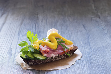 Sandwich with ham, fresh cucumber and mustard on brown paper.