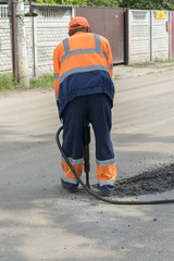 repair of roads. the worker is repairing the road. The man is working with a jackhammer. vertical photo
