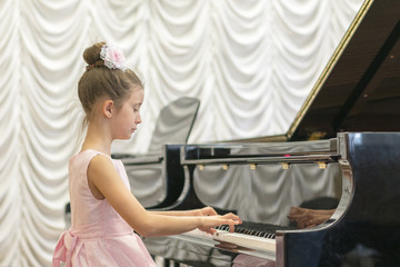 Fototapeta premium girl in a beautiful pink dress playing on a black grand piano. Girl playing on a black piano.