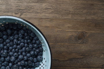 Blueberries in colander with place for text on wood table