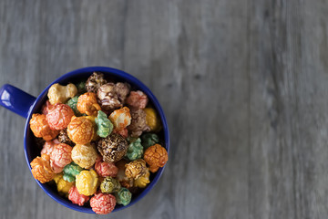 Multicolored sweet popcorn in  blue cup on gray wooden background.