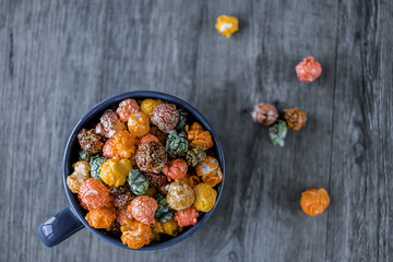 Multicolored sweet popcorn in  blue cup on gray wooden background.