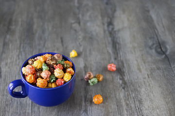 Multicolored sweet popcorn in  blue cup on gray wooden background.