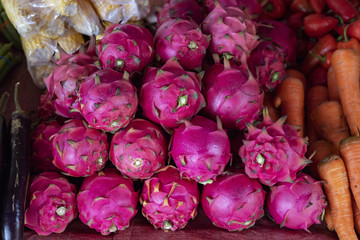 Pink dragonfruit and vegetables pile on market table. Ripe sweet dragon fruit. Colorful exotic fruit pile.