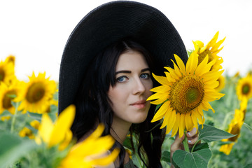 Portrait of the beautiful girl with a sunflowers. Beautiful sweet girl in dress and hat walking on a field of sunflowers, smiling. Nature, summer holidays, vacation