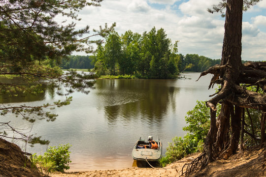 Sandy river shore with motor boat and pine trees at summer day. Russian nature river Nemda, Kostroma region.