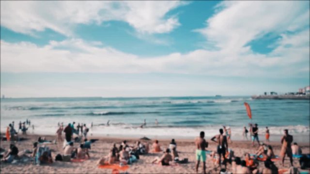 4k blured view of summer baech at Atlantic coast, Cantabrian sea, a lot of sunbathing people, colorful umbrellas, warm blue waves, orange sand and dramatic clouds on the sky