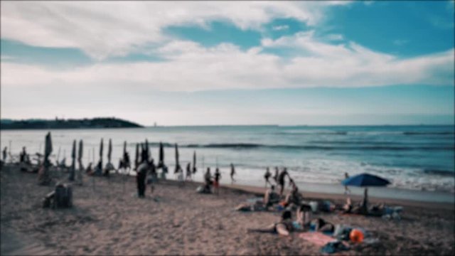 4k blured time-laps of summer baech at Atlantic coast, Cantabrian sea, a lot of sunbathing people, colorful umbrellas, warm blue waves, orange sand and dramatic clouds on the sky