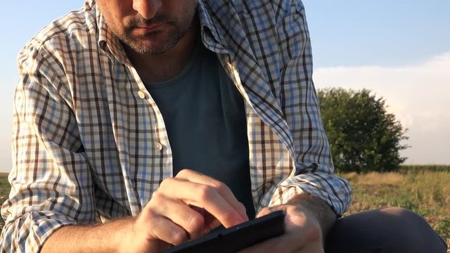 Farmer agronomist with tablet computer in bare empty field in sunset, serious confident man using modern technology in agricultural production planning and preparation