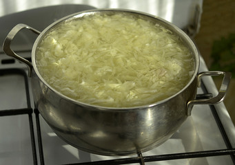 Fresh borsch cabbage soup is cooked on a gas cooker in a stainless steel saucepan.