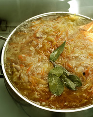 Borscht of fresh cabbage with a laurel is cooked on a gas stove in a stainless steel saucepan. Close-up.Vertical banner.