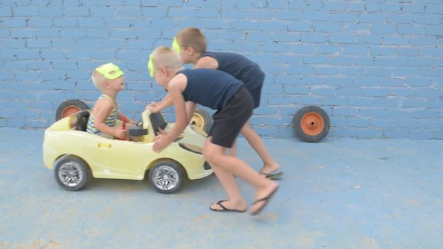 Funny kids in superhero's masks roll their little brother on yellow car. Boys are happy together and dream of adventures, travels, exploits.