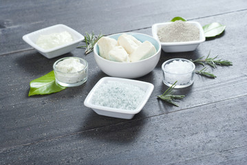 cosmetic clay powder, creams, shea butter and bath salt on old black wood table background