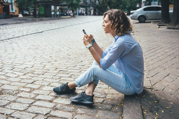 Fashionable relaxed young woman sitting on the sidewalk