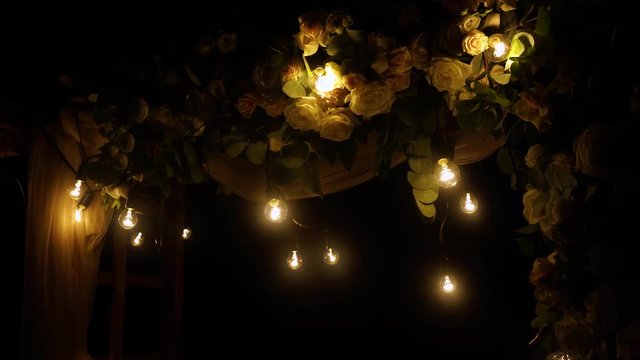 Closeup view of top of beautiful floral night wedding decorations with soft light of lamps. Outdoor reception holiday decor. Real time 4K video footage.
