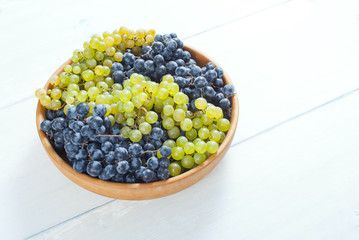 white and red grapes on wooden bowl, white wood table background