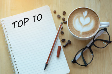 Top 10 word on notebook with glasses, pencil and coffee cup on wooden table. Business, internet,...