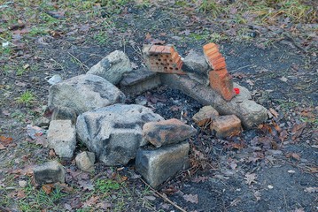 ashes of an extinct fire with bricks and stones on the ground outdoors in nature