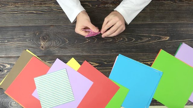 Hands making origami figure, top view. Set of colourful papers.