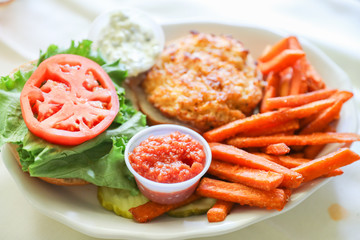 A hot, fresh, crab cake sandwich with tomato slices and sweet potato fries