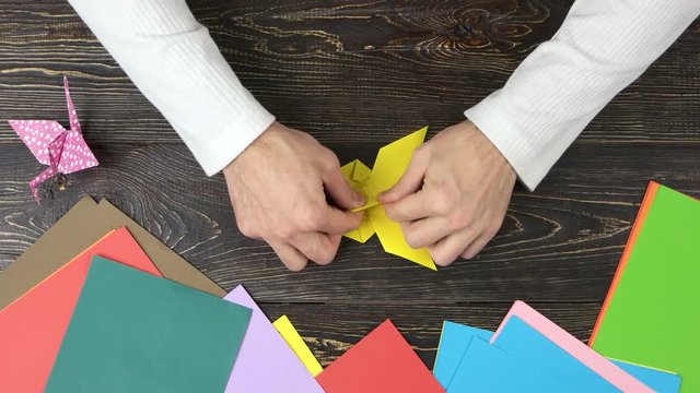 Male hands making origami butterfly. Art of origami. Top view, wooden desk surface.
