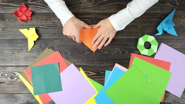 Folding origami paper in triangle, top view. Man making origami figures. Colourful papers.