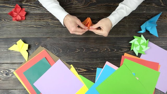 Man doing origami. Male hands folding paper sheet to make a figure on wooden table, top view.