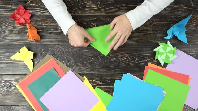 Hands of guy make origami crane with green paper. Top view, folding paper, creating figure.