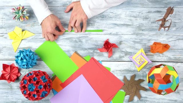 Making origami rose with stem, top view. Green origami stem, flat lay. Wooden desk surface background.