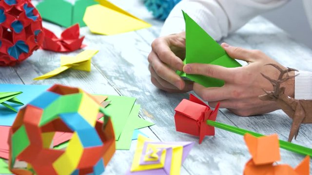 Origami crafts. Male hands making origami with green paper, close up.