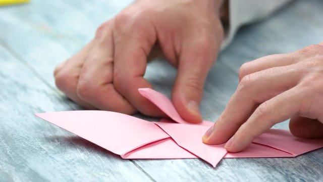 Origami crafting close up. Male hands making pink paper origami figure.