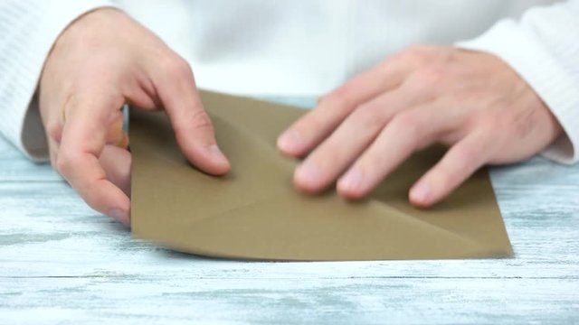 Male hands creating origami with brown paper. Extreme close up. Bright wooden table.
