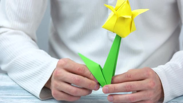 Man making yellow origami tulip. Origami flower with green stem, close up.