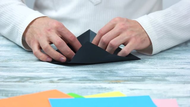 Male hands creating origami figure. Black paper for origami, close up.