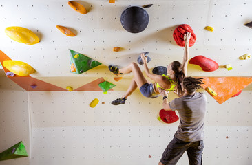 Young woman climbing bouldering problem (route), male instructor securing her