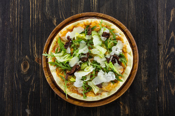 Mediterranean pizza with Parmesan cheese and dried tomatoes on wooden board