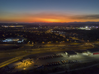 An aerial view from the drone of a neighborhood in the outskirts of Madrid city. The sunset above the mountains of Madrid with the cars passing away at the highway and the town lights start lighting